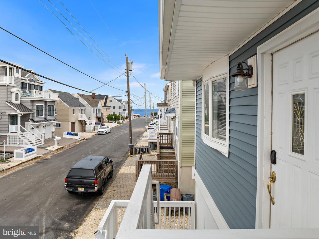 Porch view down a coastal residential street toward the ocean, with beach houses and white railings.