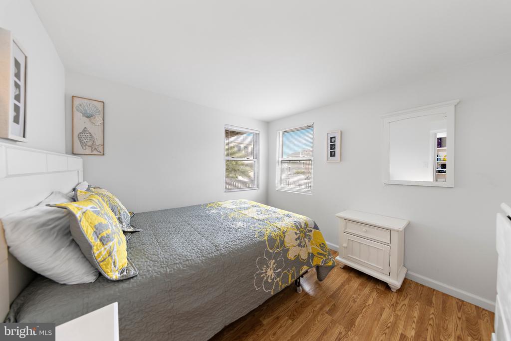 Bedroom with a gray quilted bed and yellow floral accents beside two bright windows.