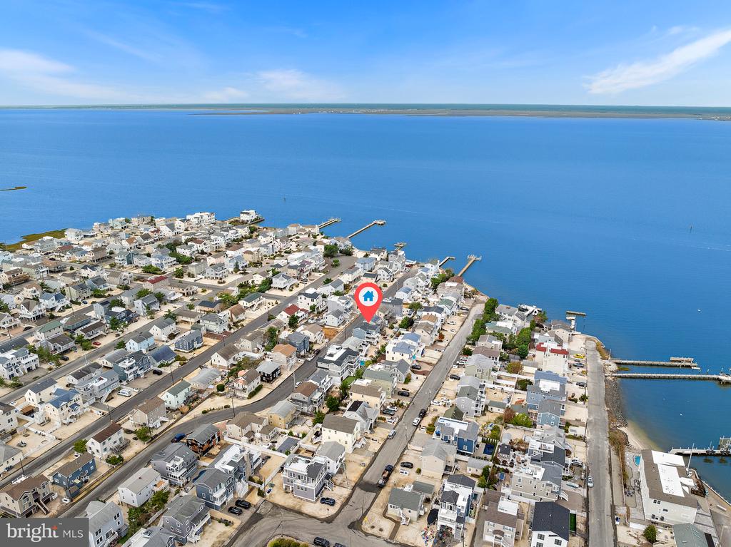 Aerial view of a coastal neighborhood beside a broad bay, with docks and a pin marking a home.