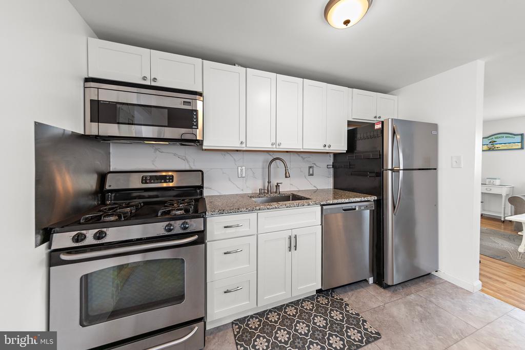 Kitchen with white cabinets, stainless steel appliances, granite counters, and a marble-look backsplash.