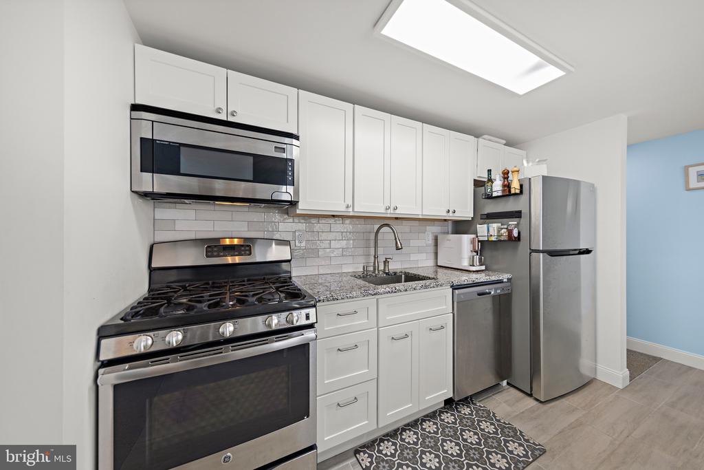 Kitchen with white cabinets, granite counters, stainless steel appliances, and a gray subway tile backsplash.