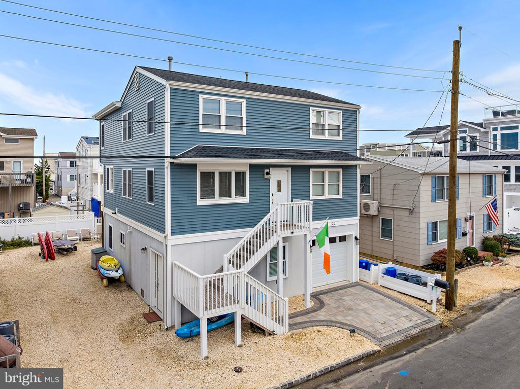 Blue two-story coastal home with white trim, elevated staircase, garage, and gravel yard.