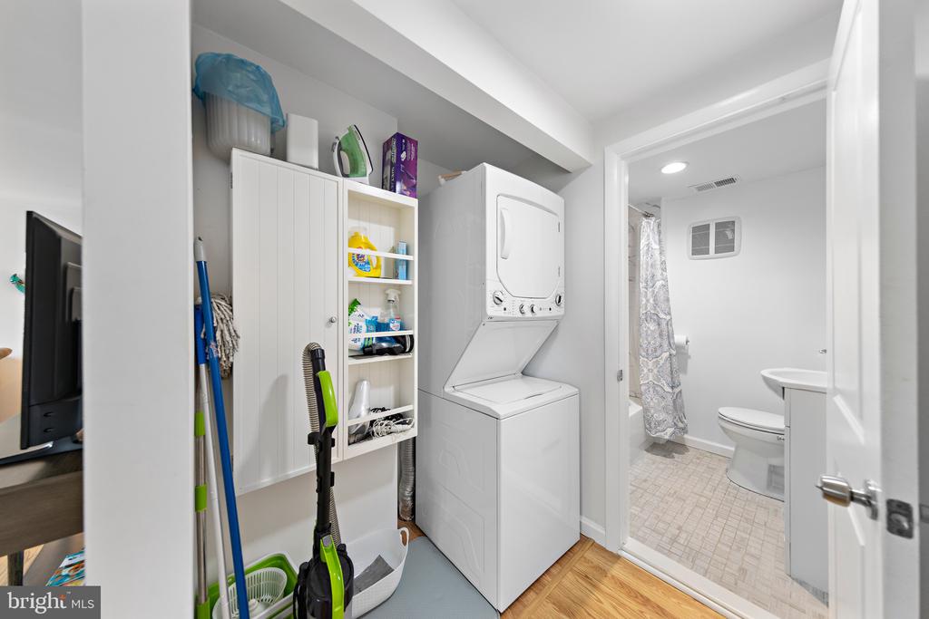 Laundry area with stacked washer and dryer, white storage cabinets, and an adjoining bathroom.