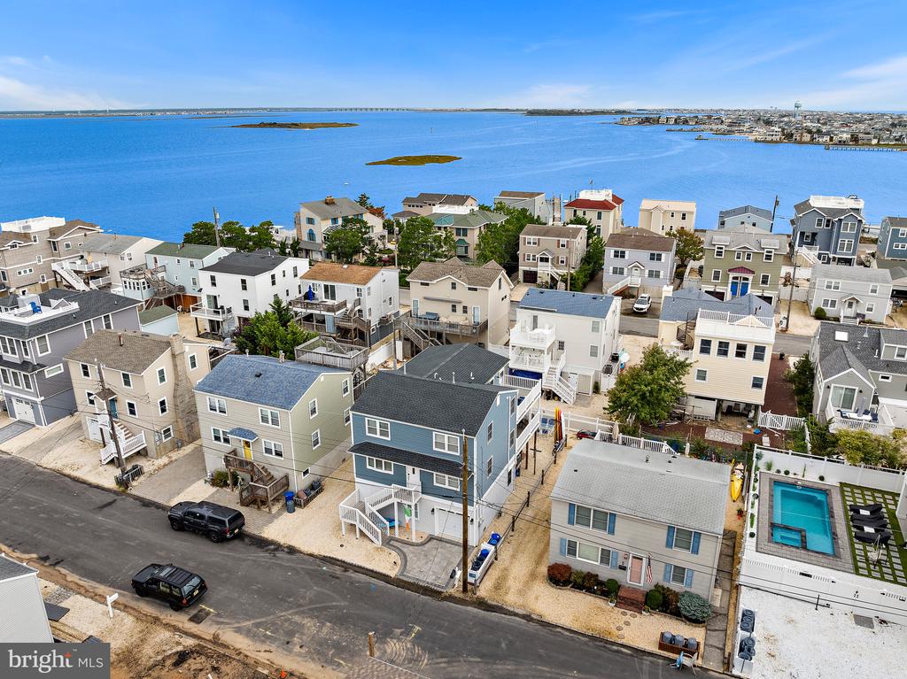 Aerial view of coastal homes beside a blue bay, with small islands and a backyard pool.