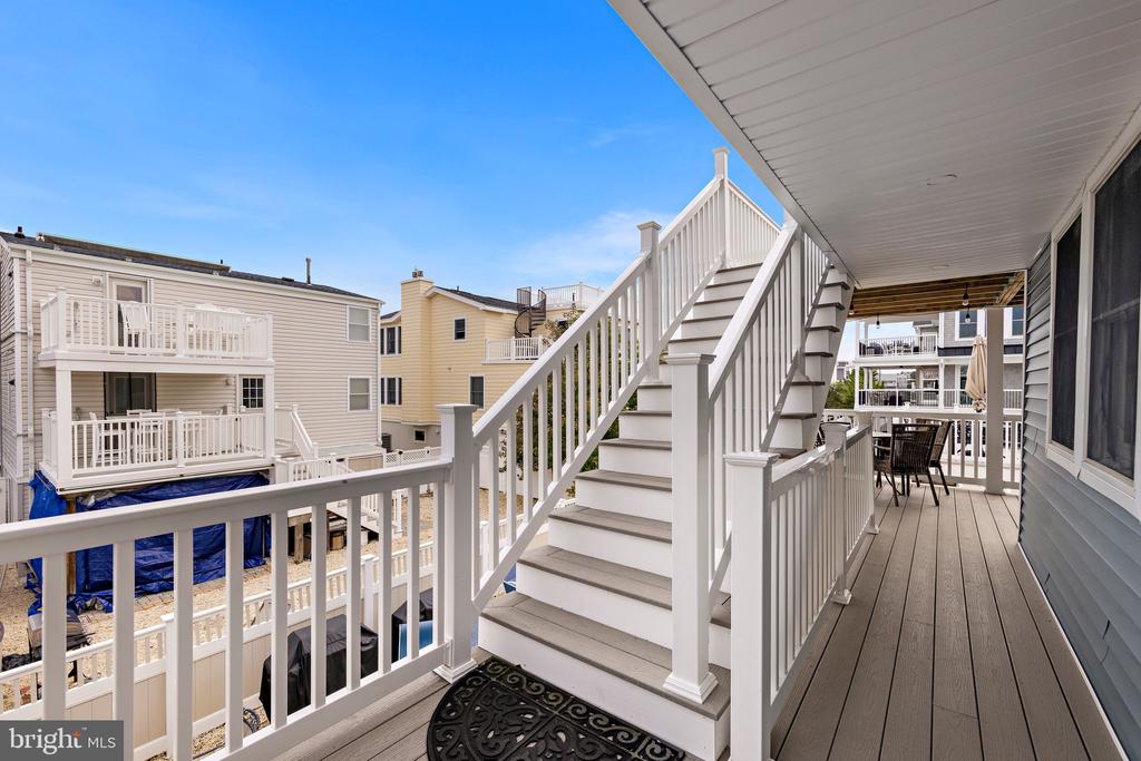 Covered deck with white staircase, railings, and outdoor dining set.