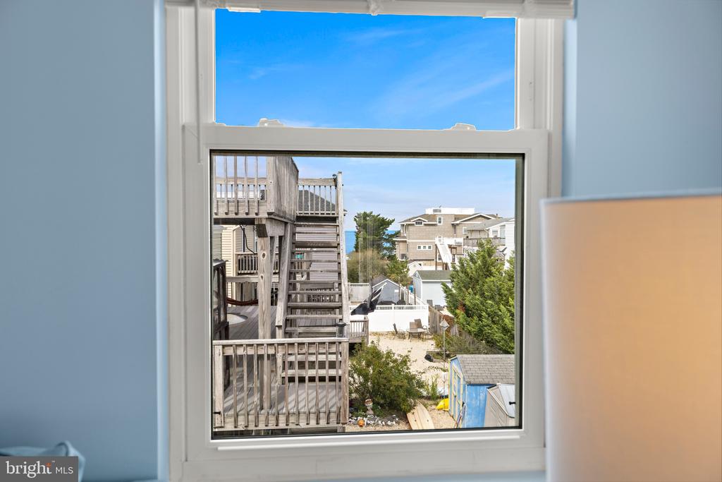 Window framing neighboring beach houses, wooden decks, and a narrow glimpse of blue water.