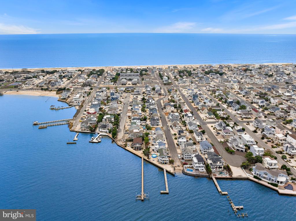 Aerial coastal neighborhood with bayfront homes, docks, beach, and ocean beyond.
