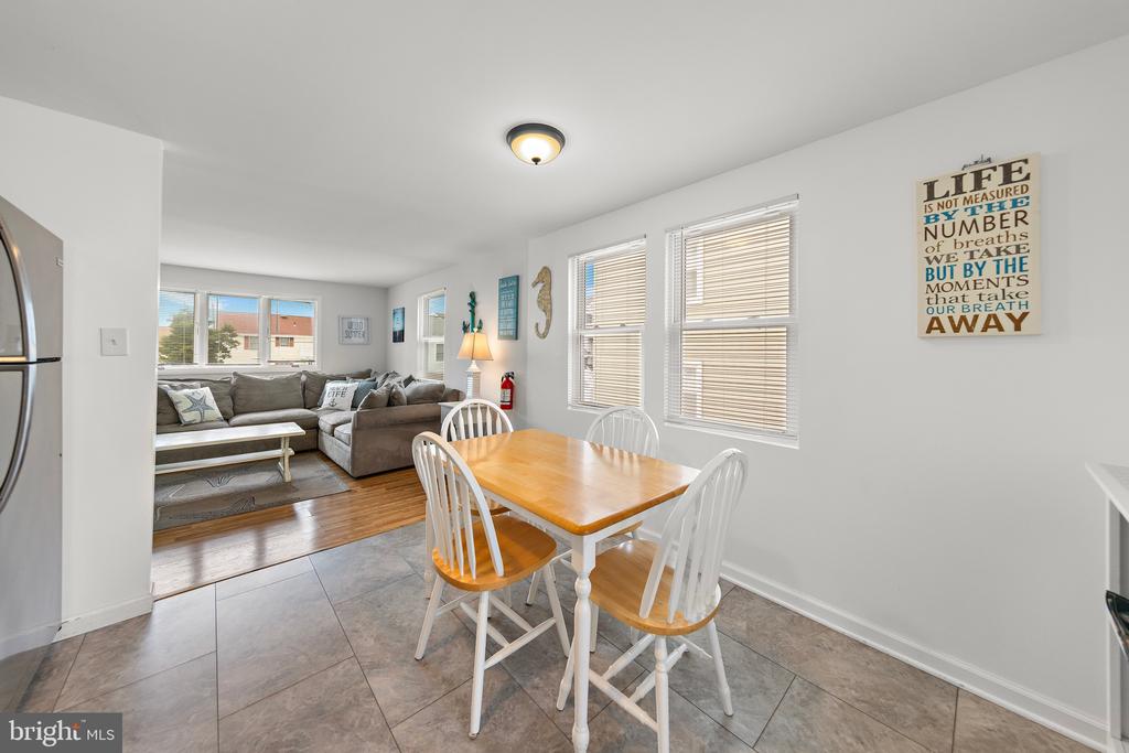 Dining area with a wooden table and white chairs opening into a living room with a gray sectional.
