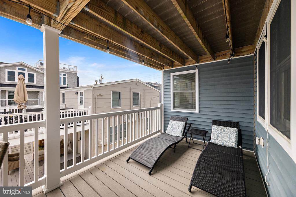 Covered deck with two lounge chairs, white railing, and views of neighboring homes.