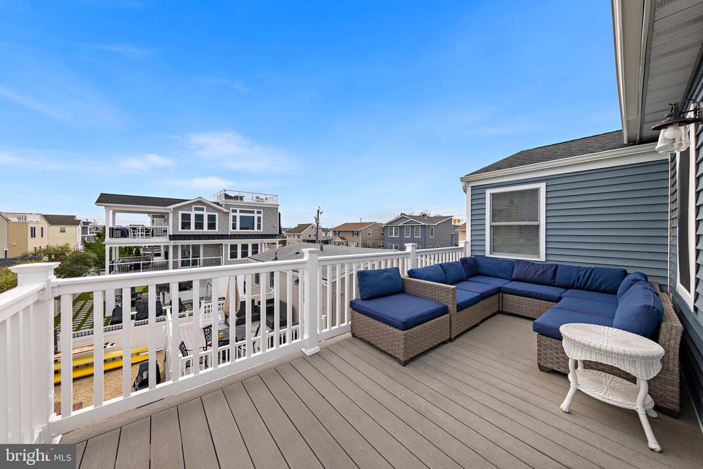 Elevated deck with blue sectional seating, white railings, and views of neighboring homes.