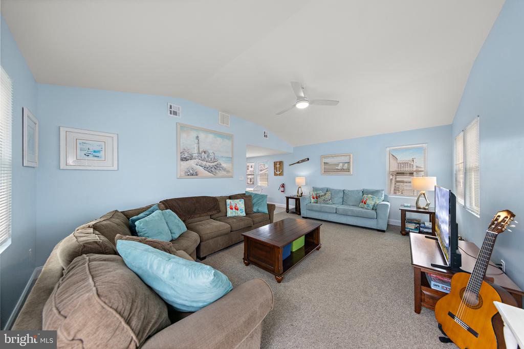Living room with blue walls, two seating areas, coastal artwork, and a guitar beside the television.