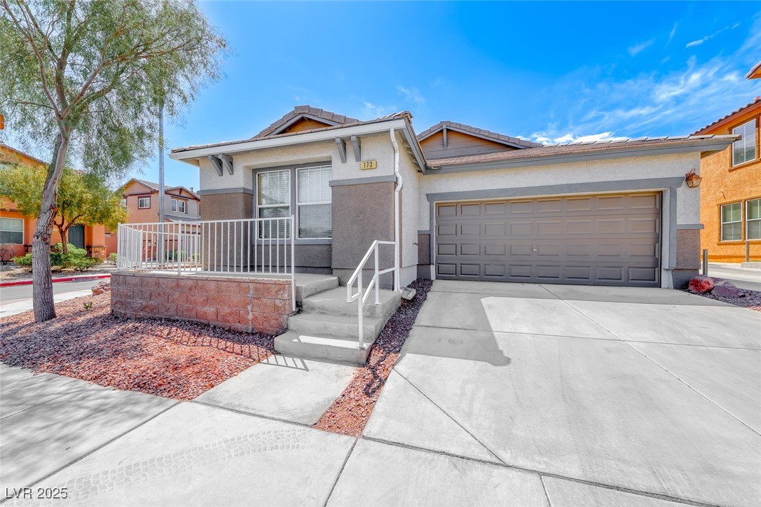 Single-story gray stucco home with a two-car garage, broad driveway, and raised front entry.