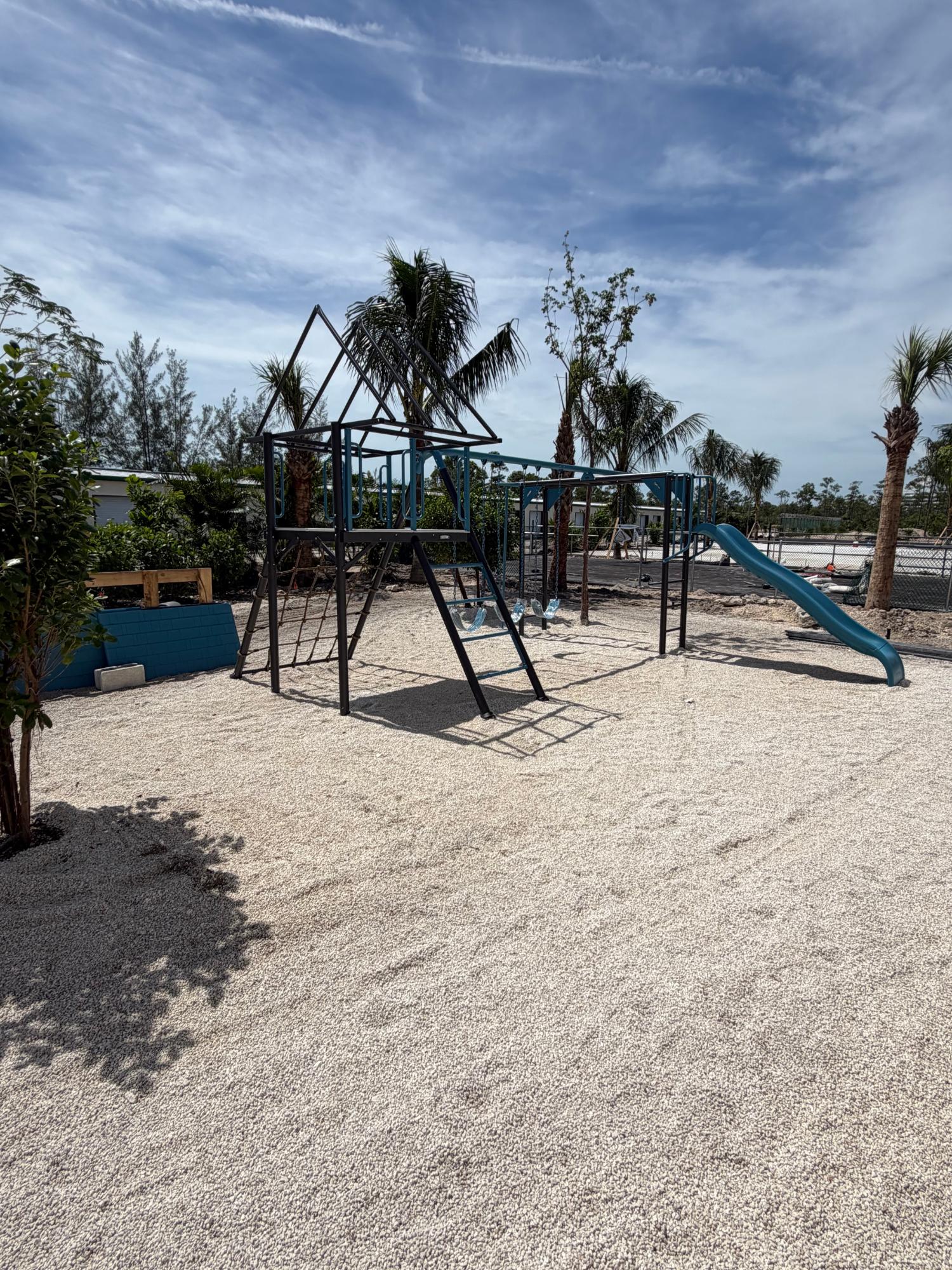 Outdoor playground with a climbing frame, swings, and blue slide on a gravel surface.
