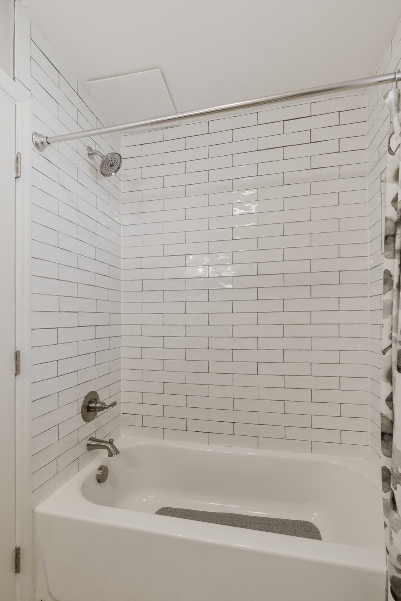 White tub and shower with glossy subway tile and chrome fixtures.