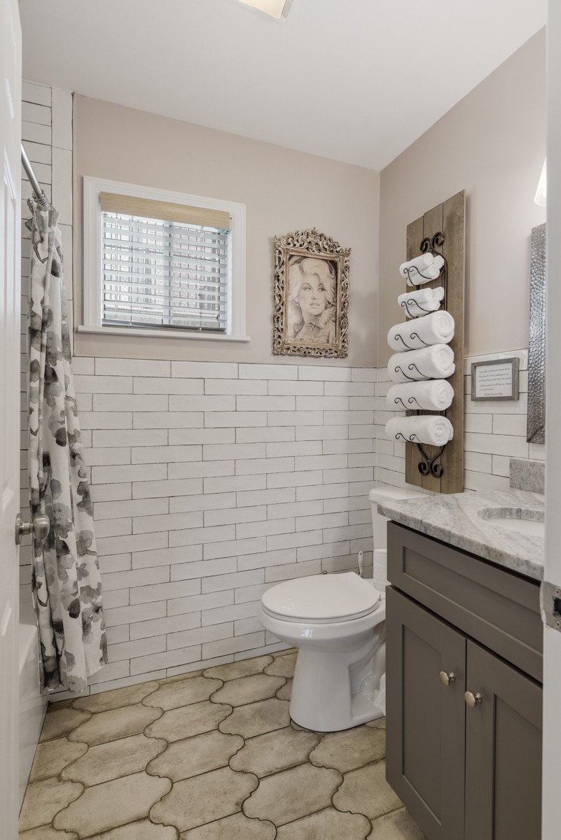 Bathroom with white tiled walls, a gray vanity, patterned floor, and a wall-mounted towel rack.