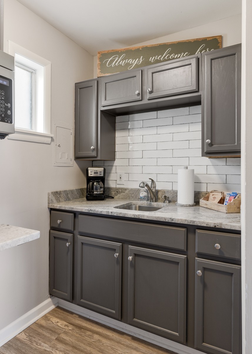 Kitchen with dark gray cabinets, white tile backsplash, stone counters, and a coffee maker.
