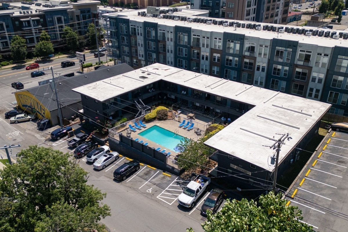 Aerial view of an apartment complex with a turquoise courtyard pool and surrounding parking lot.