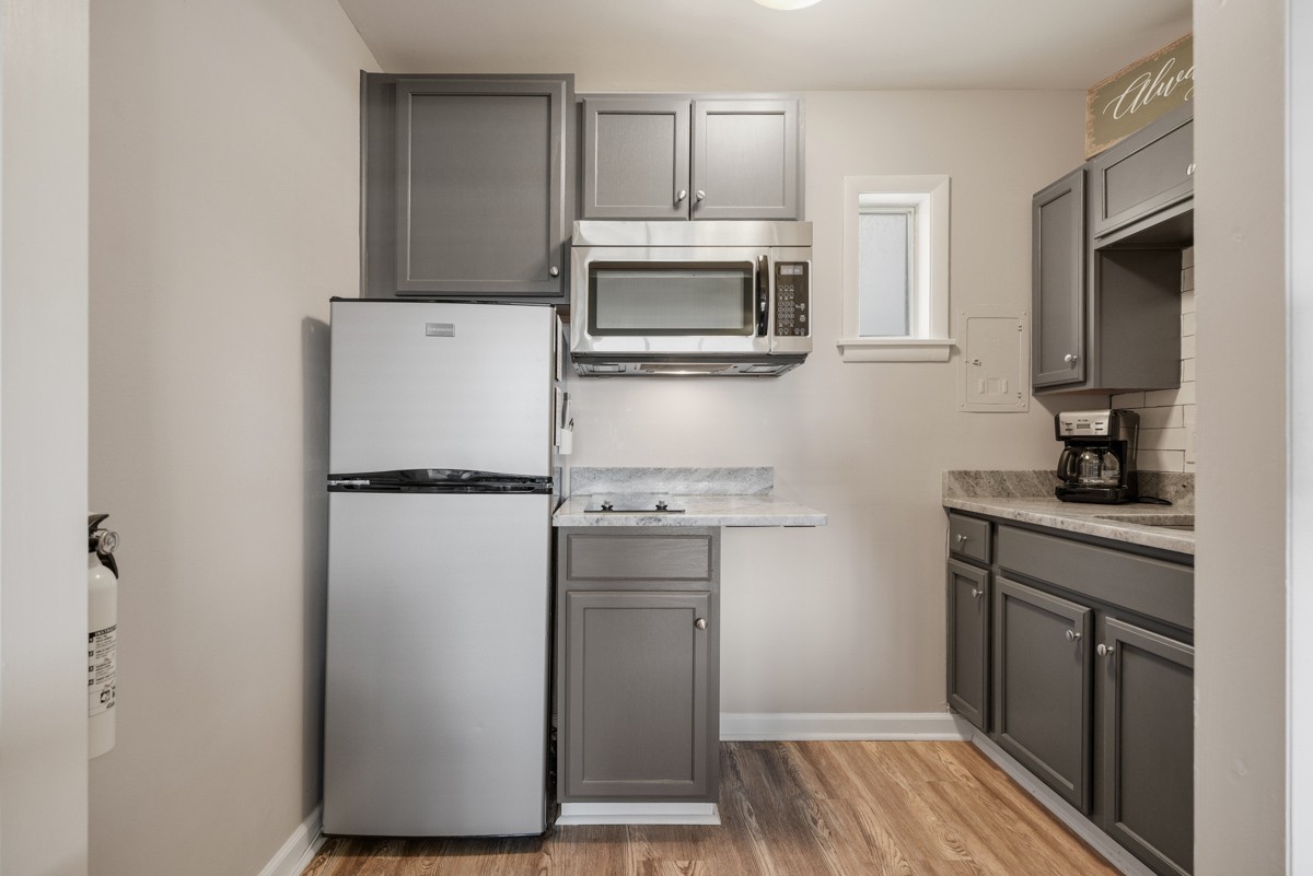 Compact kitchen with gray cabinets, stainless-steel appliances, stone-look counters, and wood-look flooring.