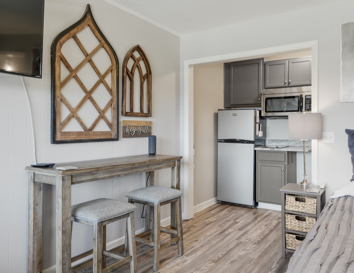 Furnished studio interior with a gray kitchenette, refrigerator, microwave, and rustic console table.