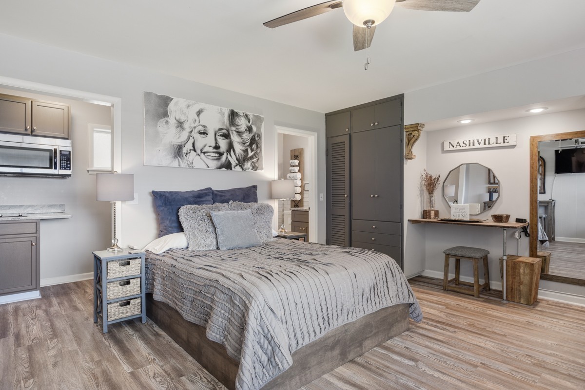 Furnished bedroom with a gray bed, kitchenette, dark built-in cabinets, and a vanity table.