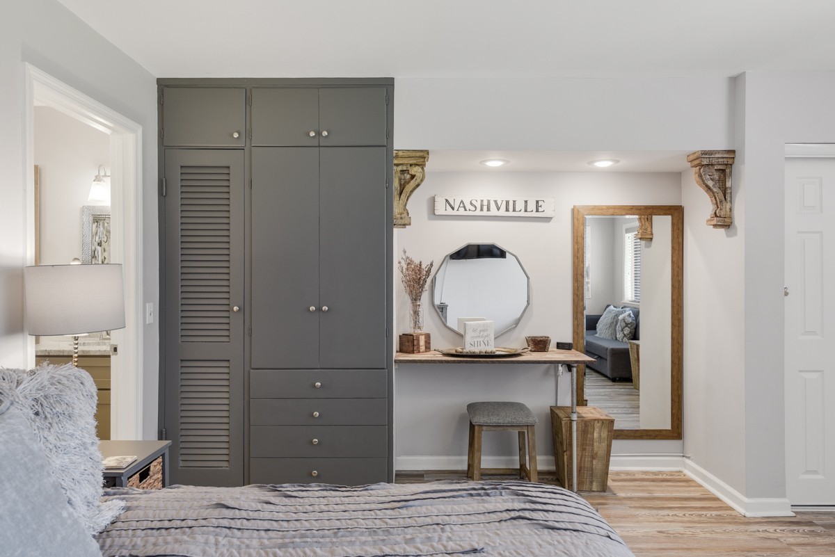 Staged bedroom with charcoal built-in wardrobe, vanity, octagonal mirror, and Nashville wall sign.