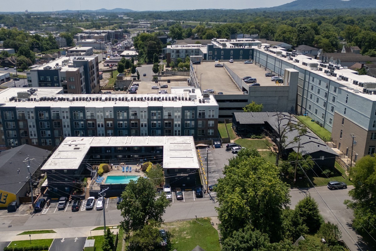 Aerial view of apartment buildings surrounding a courtyard pool, with wooded hills in the distance.