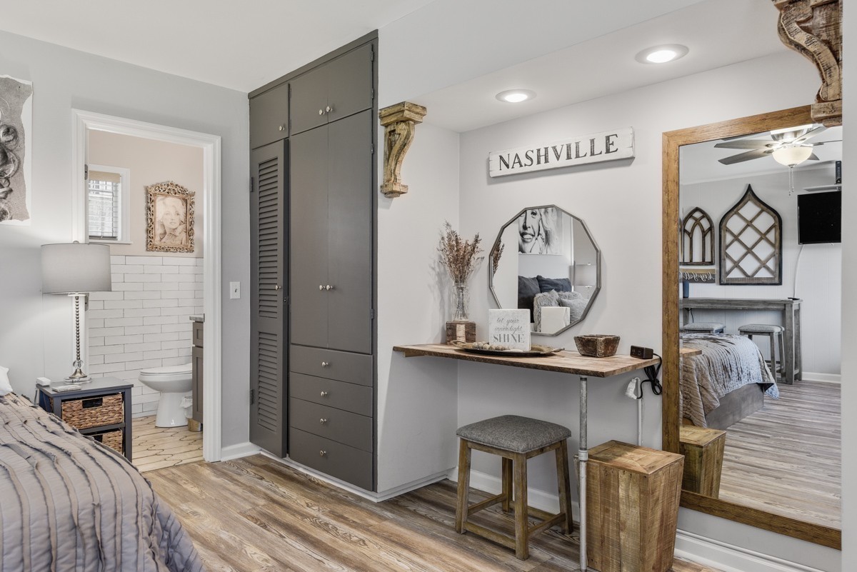 Staged bedroom with a dark built-in wardrobe, console table, and doorways to a bathroom and another bedroom.
