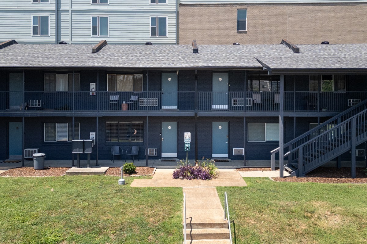 Two-story condominium building with dark blue siding, shared balconies, and a central walkway.