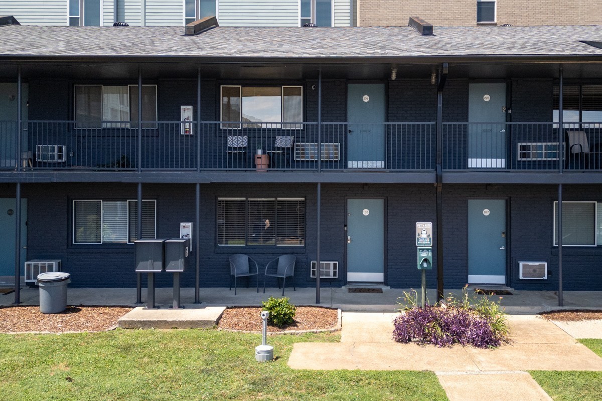 Two-story dark-brick condominium building with covered walkways, blue unit doors, and a front lawn.