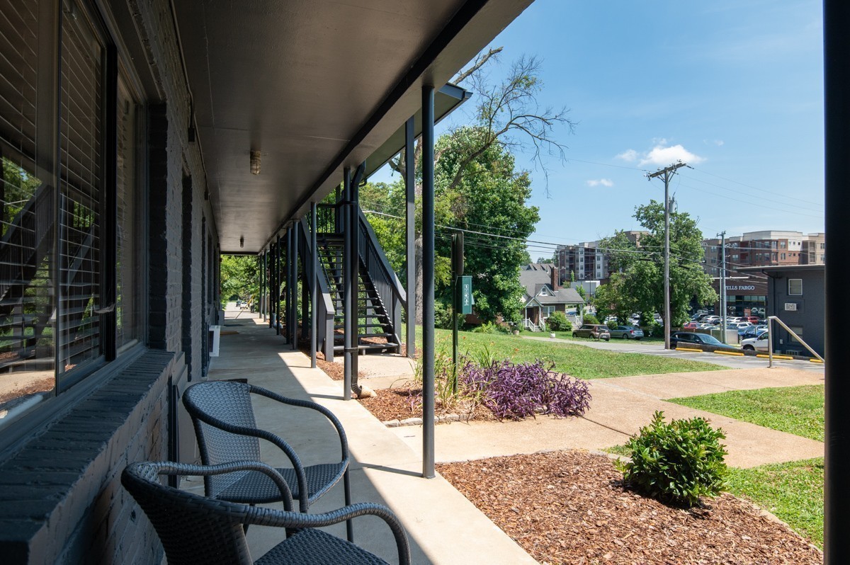 Covered residential walkway with wicker chairs, exterior stairs, and landscaped grounds.