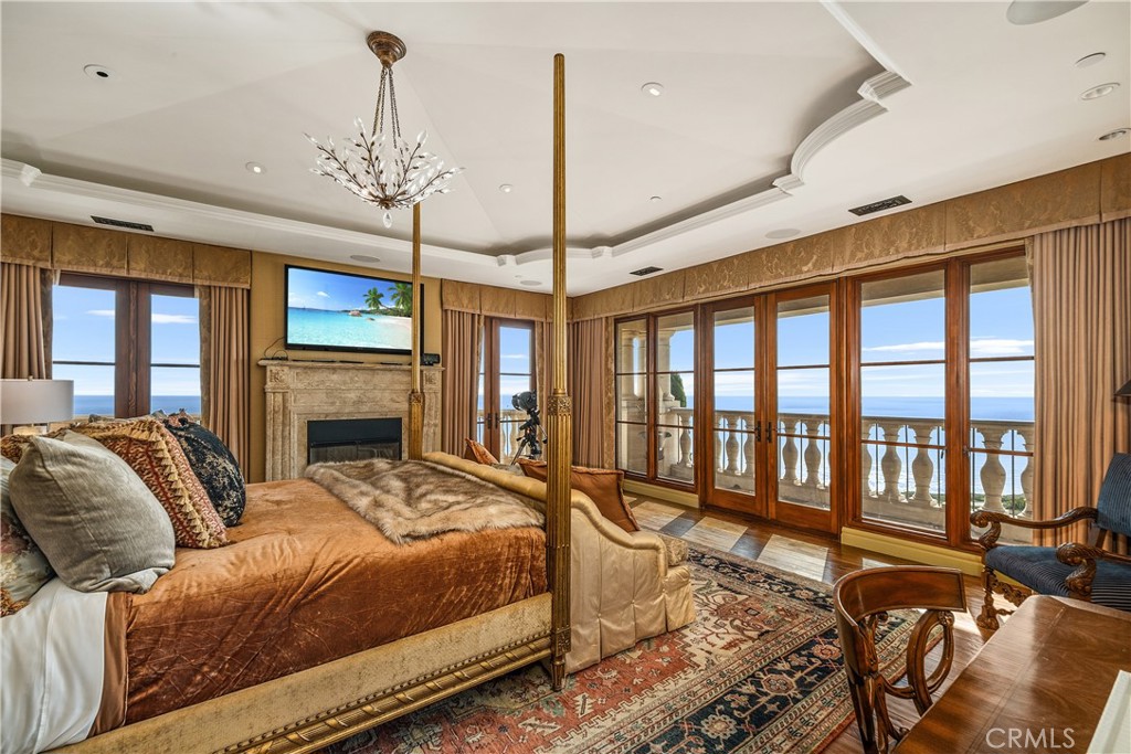 Bedroom with an ornate four-poster bed, fireplace, and ocean views through tall windows.