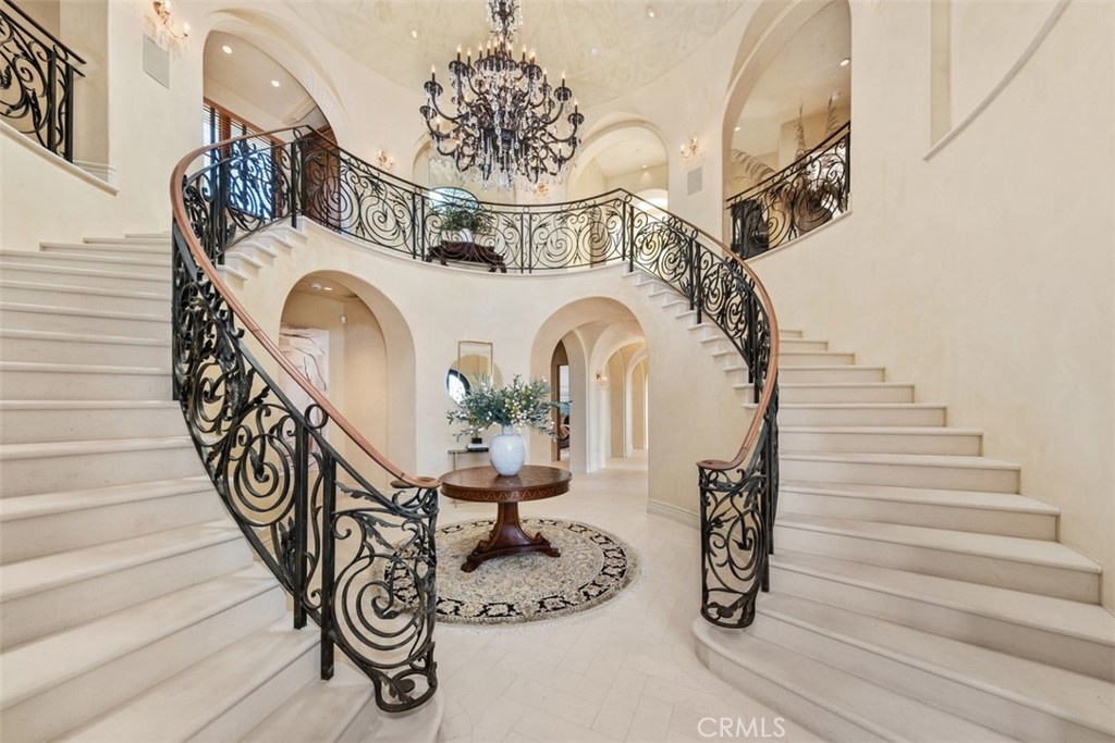 Grand foyer with a sweeping double staircase, ornate iron railings, and a chandelier.