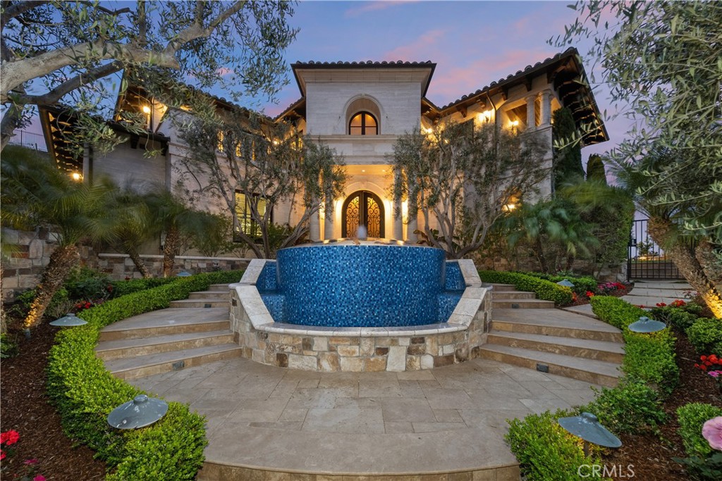 Mediterranean-style home with illuminated entry behind a blue-tiled fountain and terraced steps.