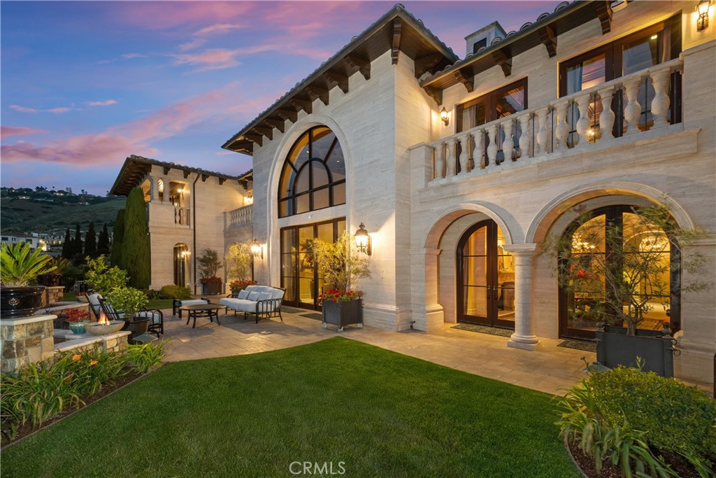 Stone home with arched windows, a balcony, and a furnished patio at dusk.