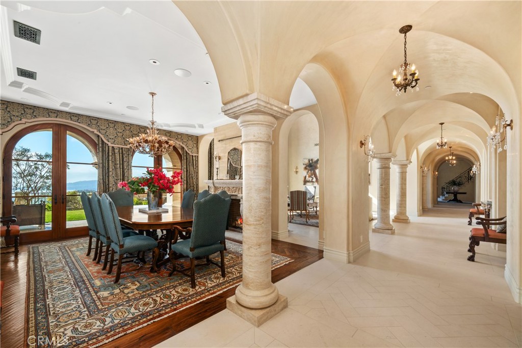 Dining room with arched glass doors, patterned rug, and a view into a columned hallway.