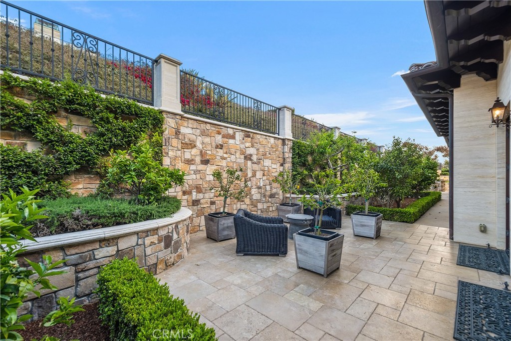 Stone courtyard patio with wicker seating, potted trees, and landscaped raised beds.