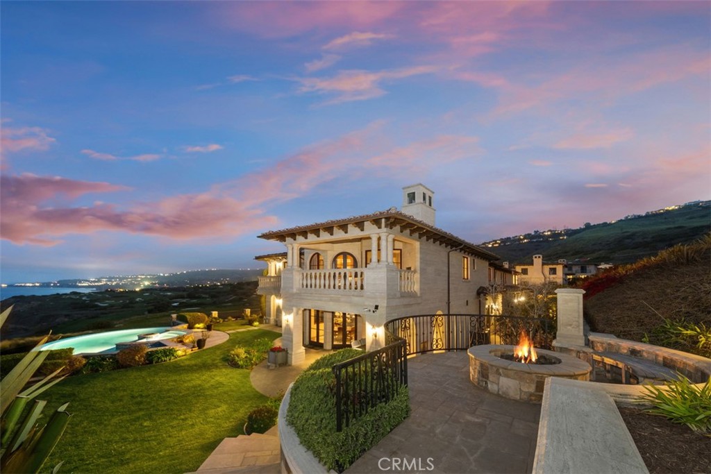 Mediterranean-style home with a pool, ocean views, and a fire pit at dusk.