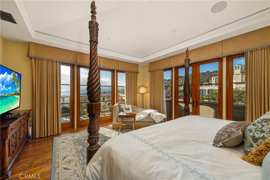 Furnished bedroom with carved wood posts and tall windows overlooking a balcony and water views.