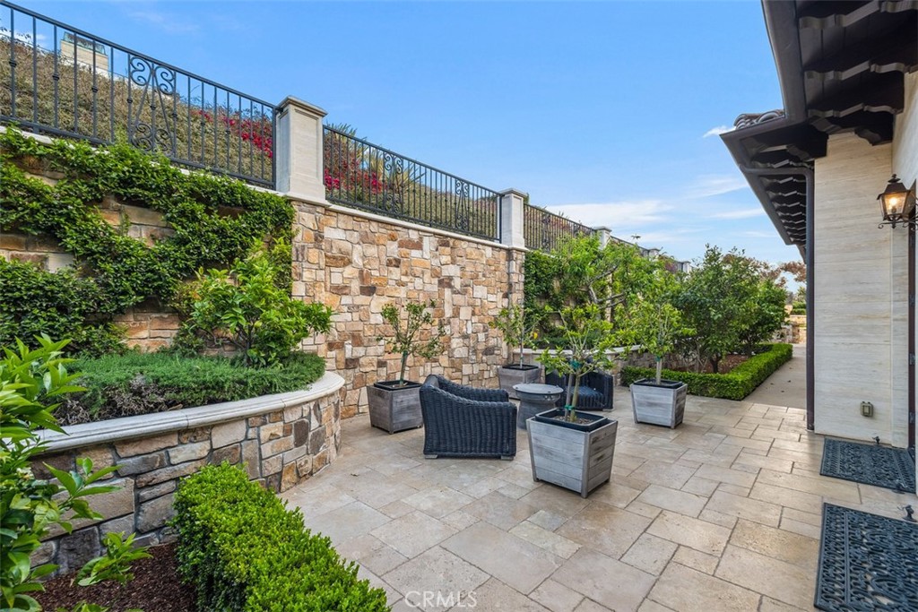 Stone-paved patio with wicker seating, planters, and a landscaped stone wall.
