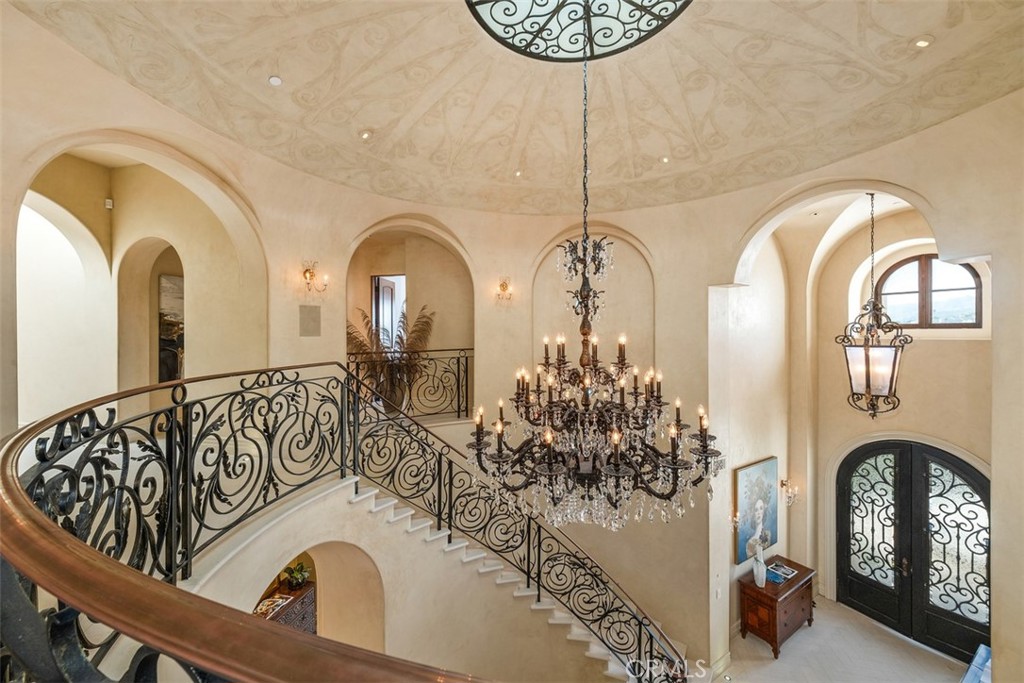Two-story foyer with a sweeping wrought-iron staircase and large crystal chandelier.