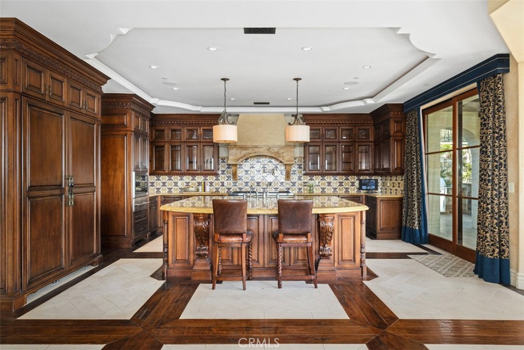 Kitchen with dark wood cabinetry, a large island, decorative tile backsplash, and glass doors to an outdoor area.