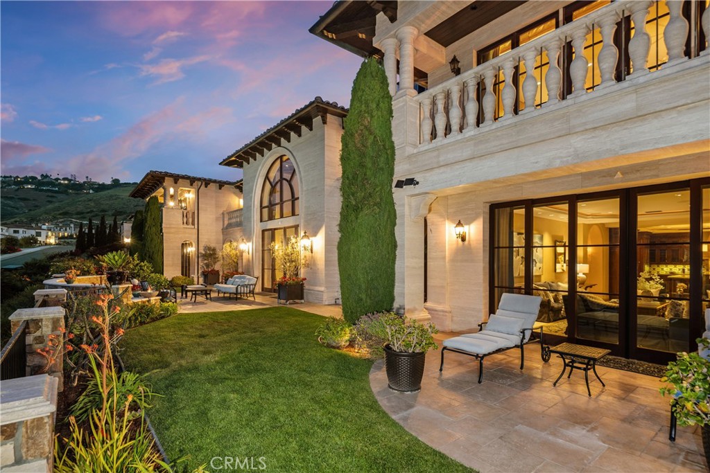 Stone home at dusk with an arched window, balcony, and lawn patio seating.
