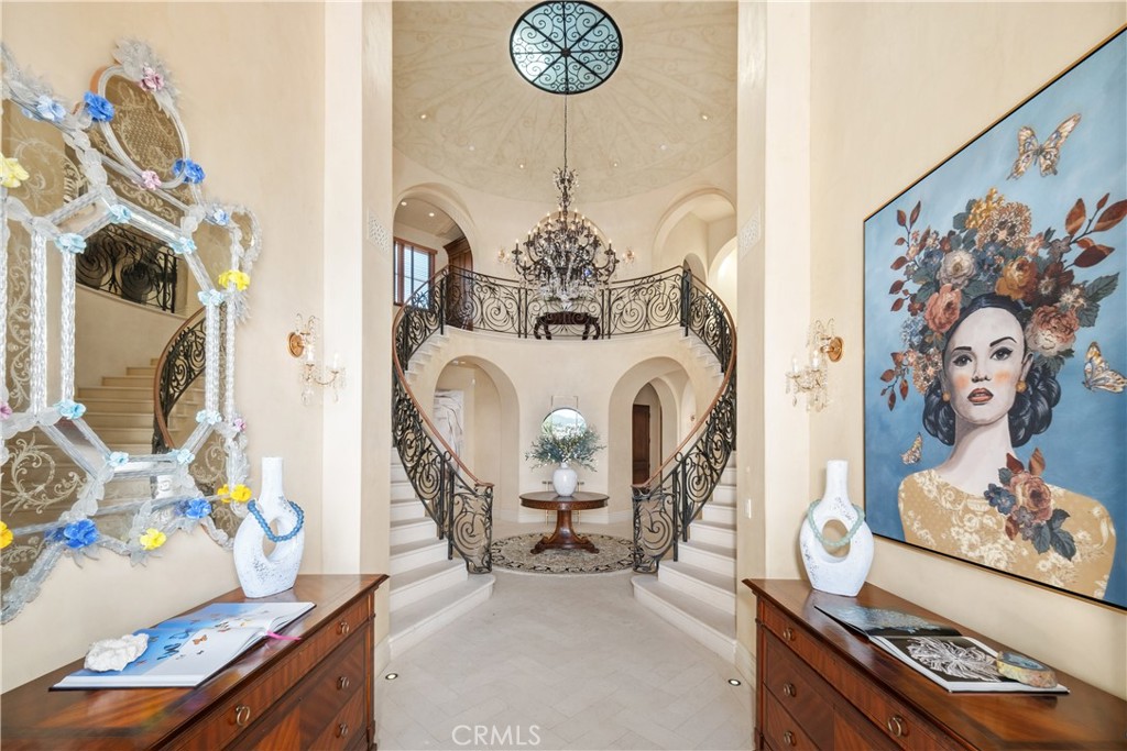 Grand foyer with a sweeping double staircase, ornate iron railings, and a chandelier.