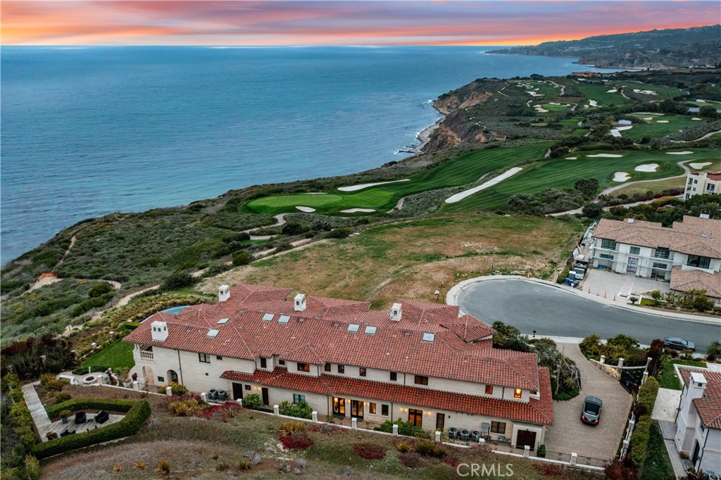 Coastal home with a red tile roof overlooking the ocean and seaside golf course at dusk.