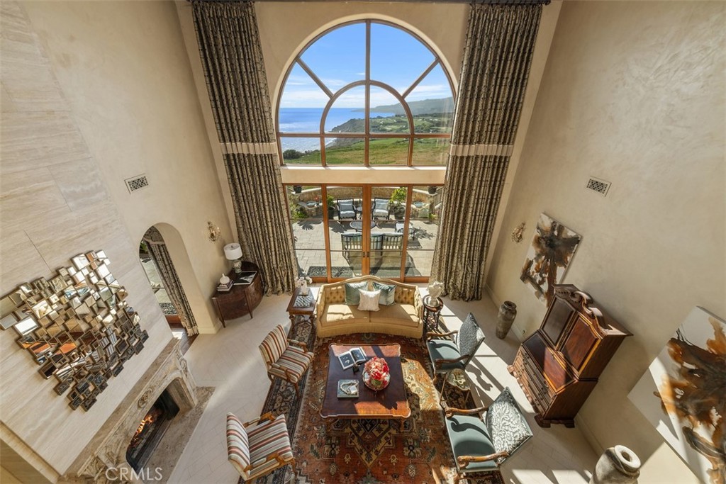 Two-story living room with an arched ocean-view window, fireplace, and patterned rug.
