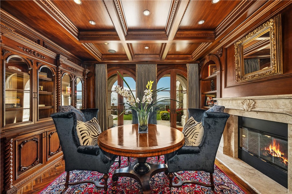 Formal sitting room with carved wood cabinetry, a coffered ceiling, arched windows, and a lit stone fireplace.