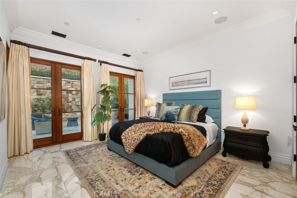 Staged bedroom with teal bed, marble flooring, and French doors opening to a stone-walled patio.