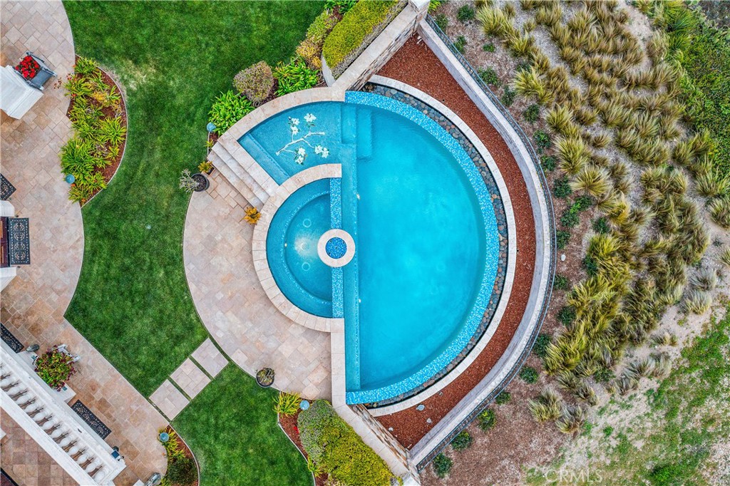 Aerial view of a curved pool and circular spa beside stone patios and landscaped grounds.