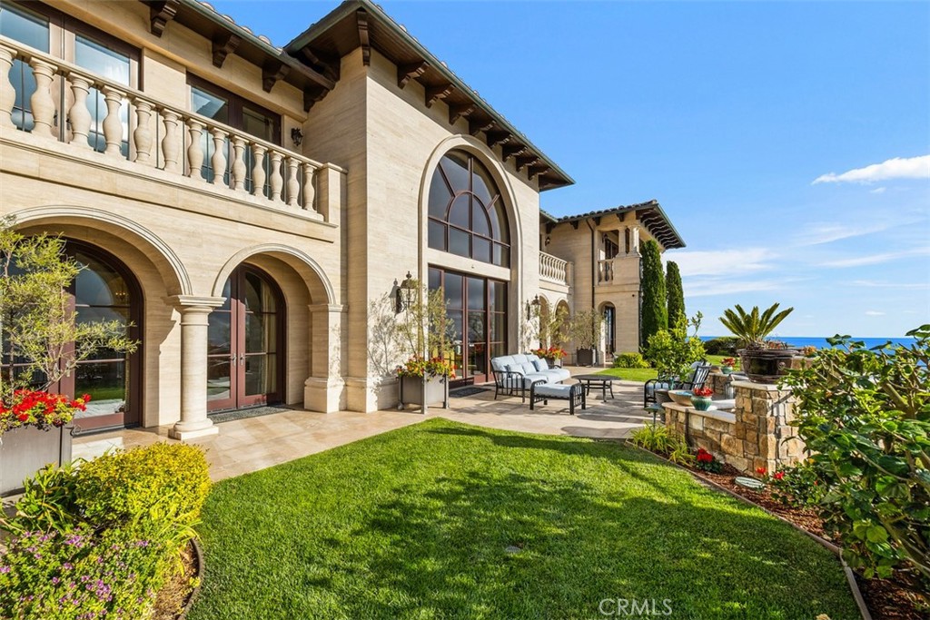 Stone home with arched windows, a furnished patio, landscaped lawn, and ocean view.