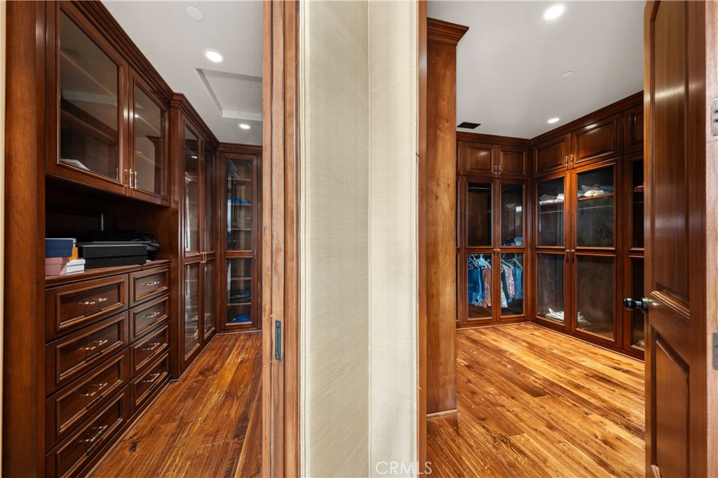 Walk-in closet with dark wood built-ins, glass-front wardrobes, and polished hardwood floors.